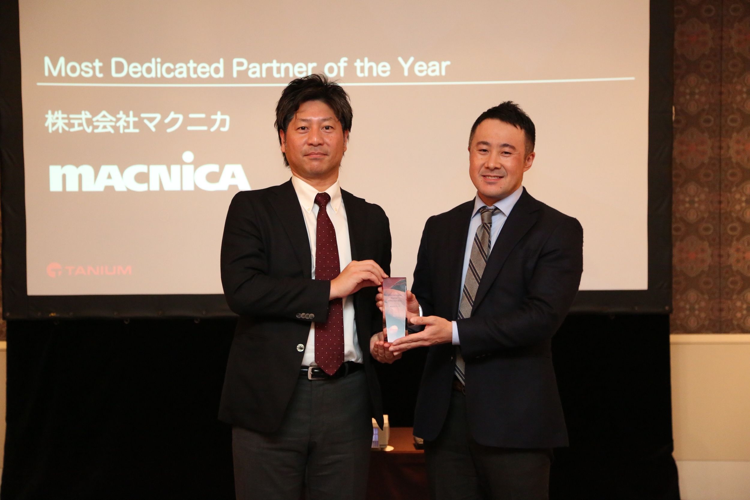Two men presenting award on stage with Most Dedicated Partner of the Year displayed