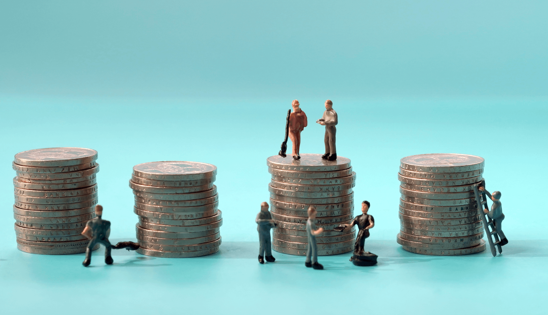 ミニチュアの労働者のフィギュアが銀貨のタワーの隣に立っている。