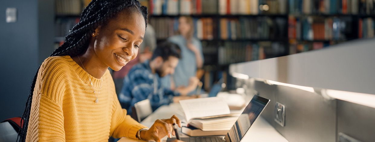 大学図書館:才能ある黒人女子学生がノートパソコンを使用してノートを書く