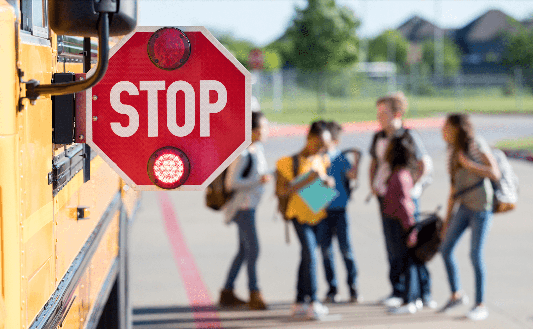 ブログの画像。 ピントが合っていない中学生が近くでおしゃべりしている、スクールバスの横に付いているSTOPサインの写真。