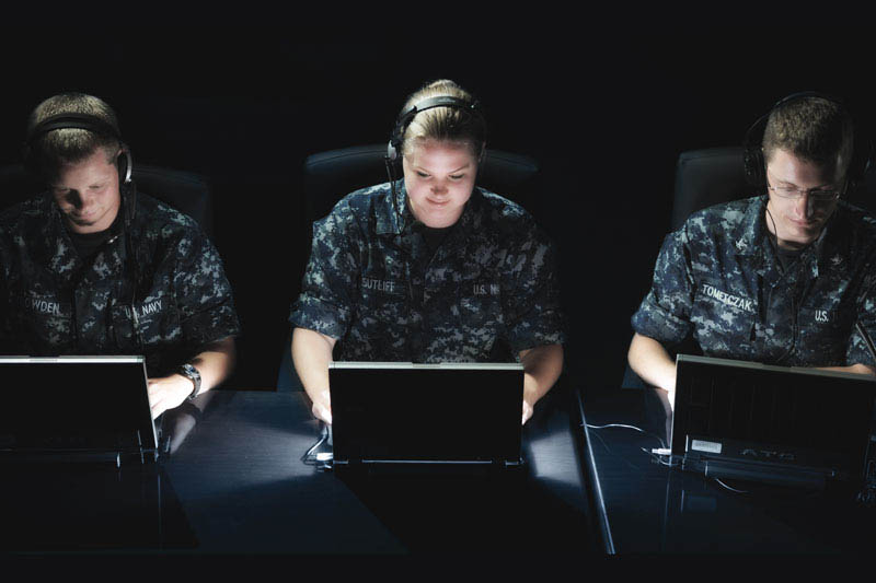 制服を着た海軍の隊員3人が、コンピューターの前で作業しています
