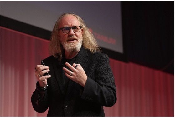 Man with long gray hair speaking at conference presentation