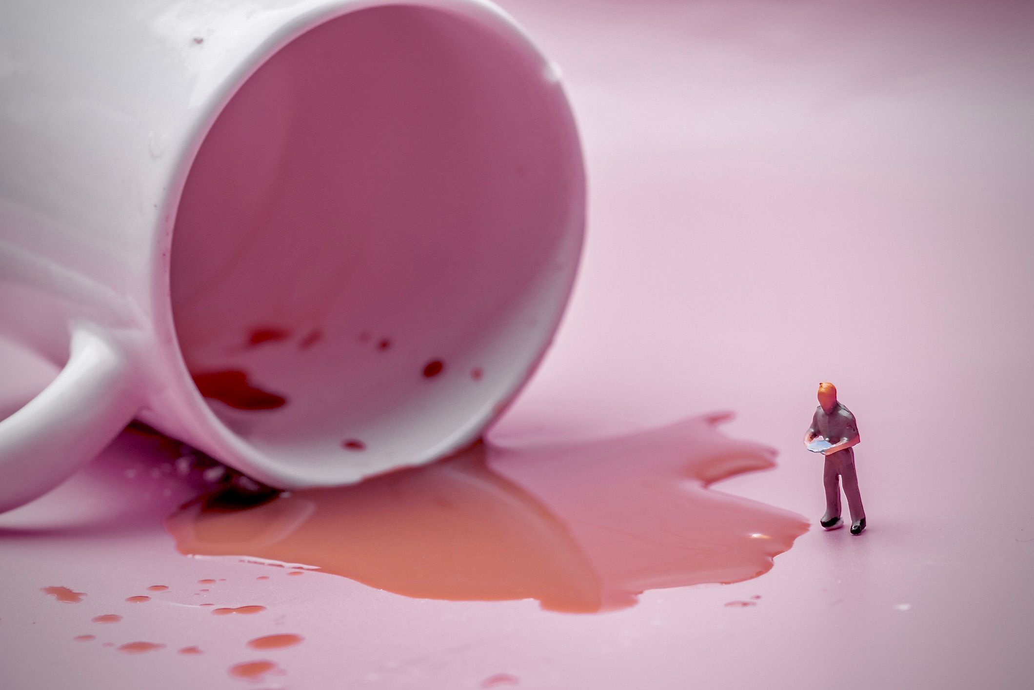 ひっくり返ったマグカップからこぼれたコーヒーを調べているミニチュアの人物像の画像。