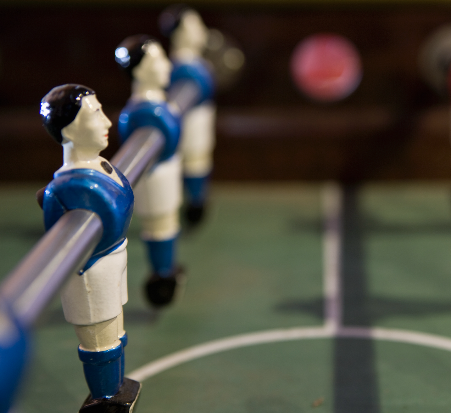 Closeup image of a foosball table, with plastic figures on a metal rod wearing blue jerseys.