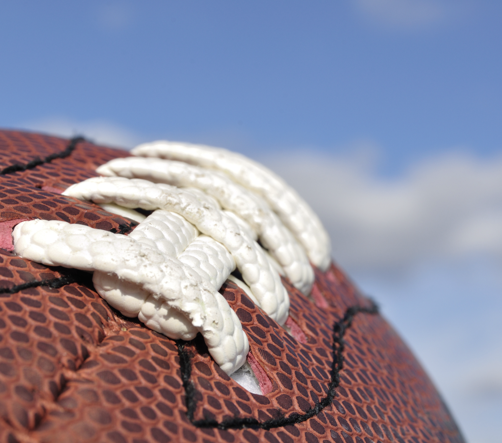 Closeup photo of a brown football with white laces and a blue sky beyond.